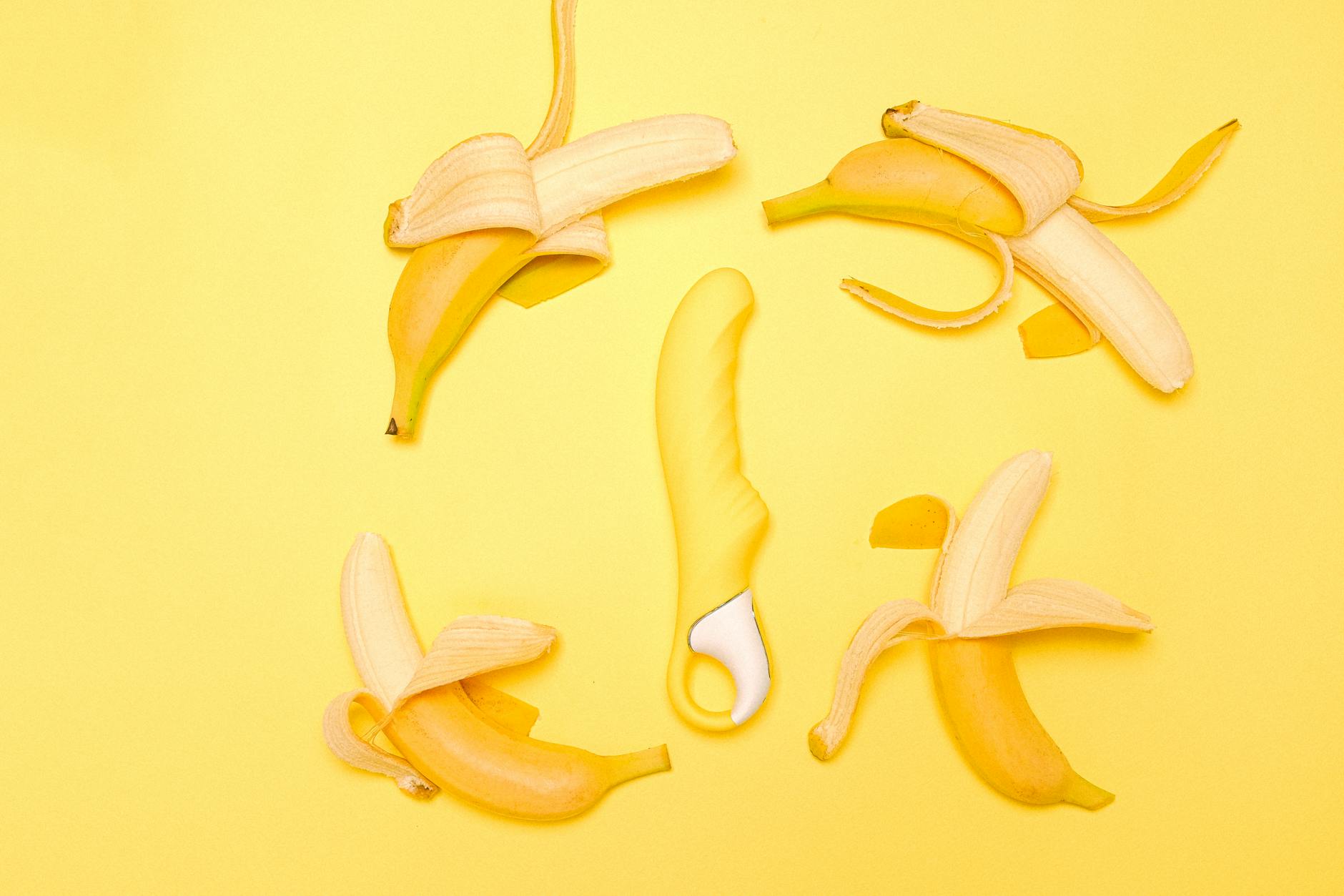 A yellow silicone lemon clitoral vibrator on a bright yellow background with fresh lemons