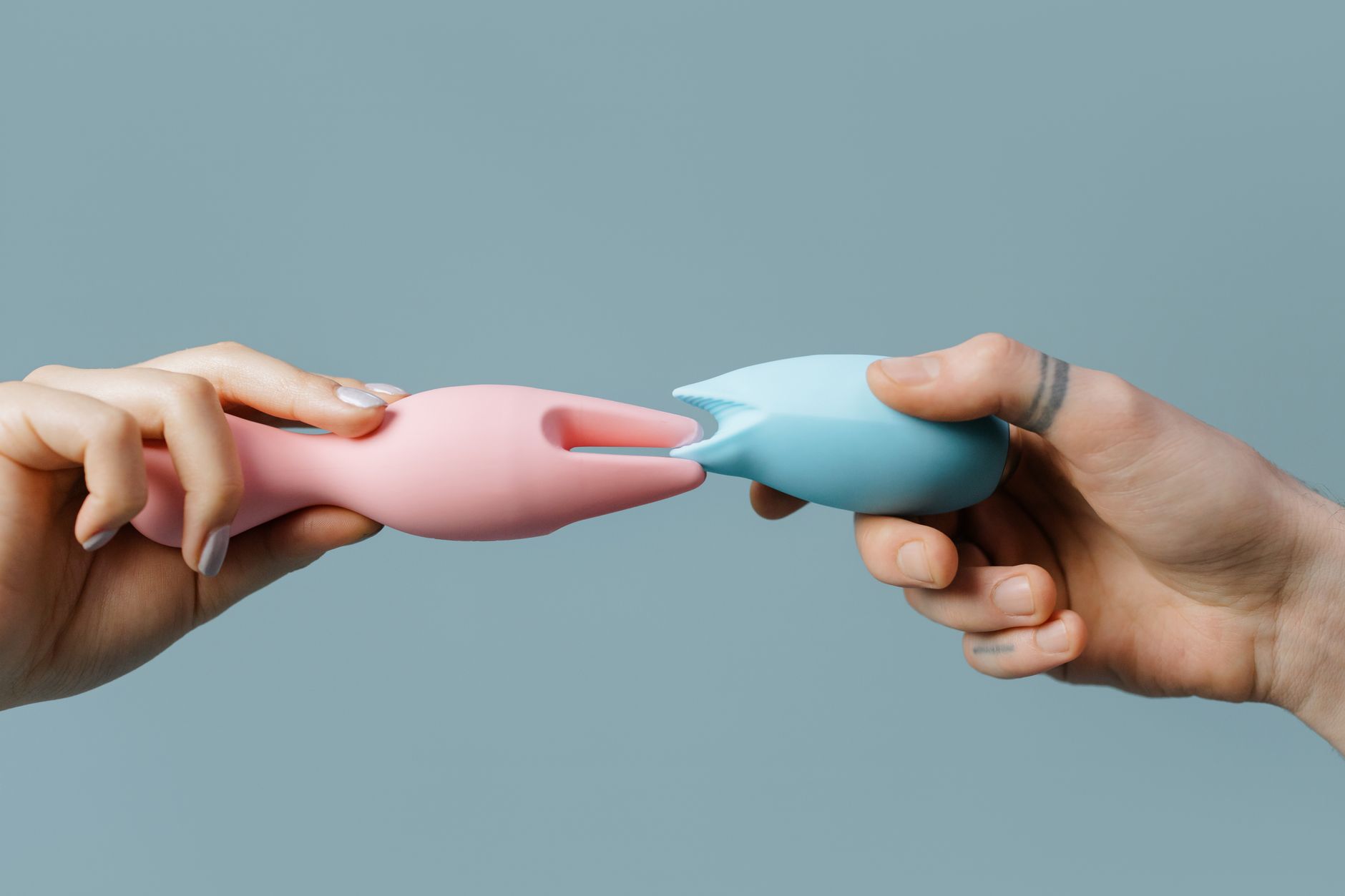 Hands holding pastel-colored silicone toys and clitoral vibrators for pleasure