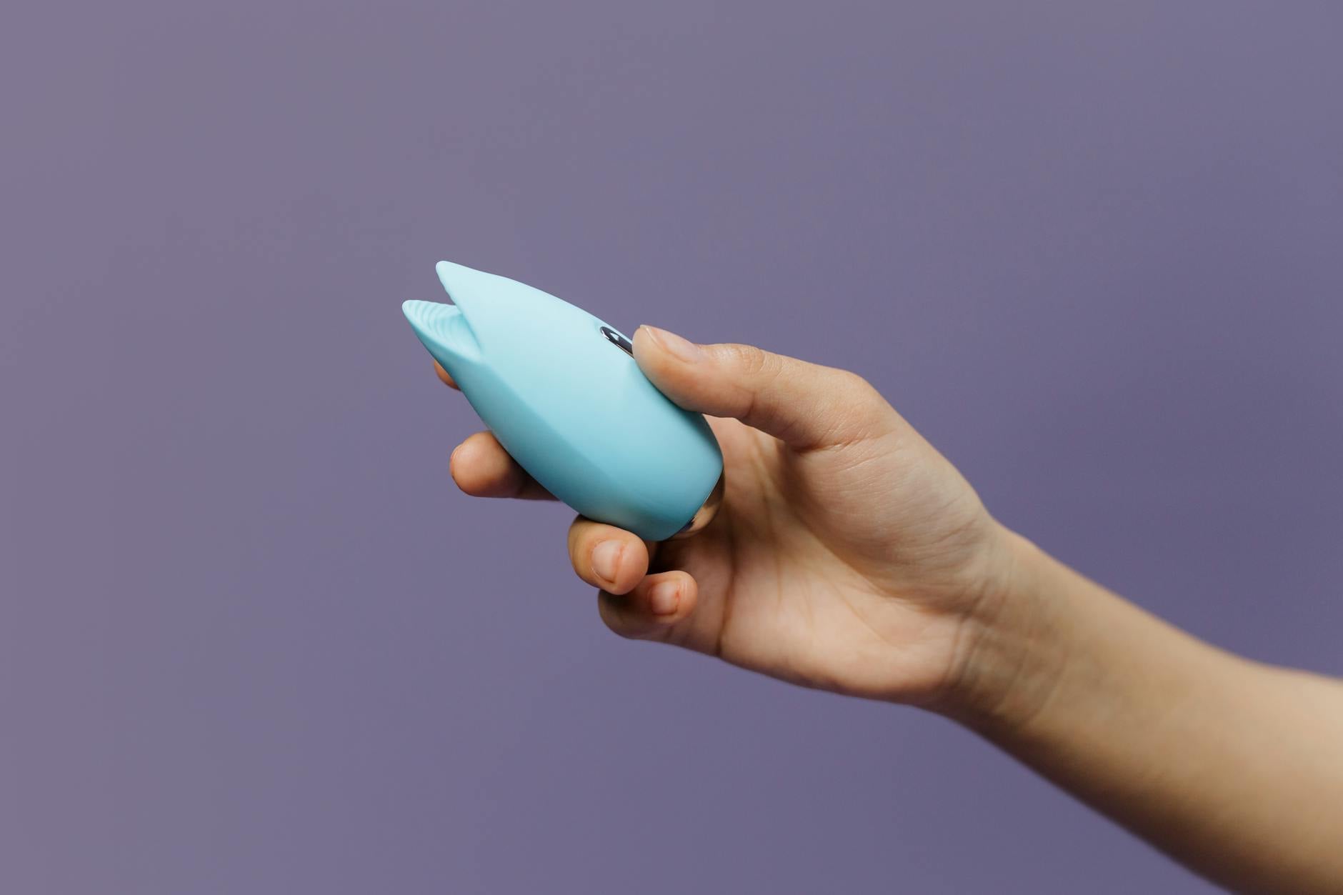 A blue silicone lemon vibrator held in hand against a purple background, designed for clitoral stimulation