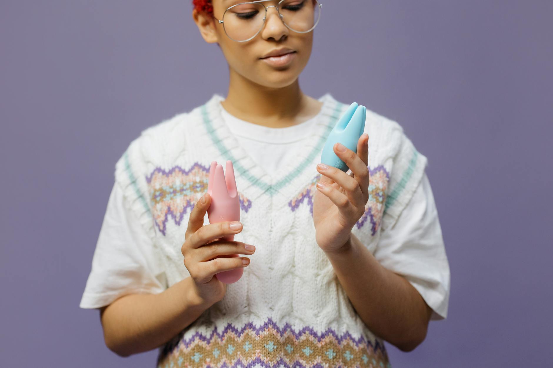 Woman holding blue and pink silicone vibrators, demonstrating different clitoral stimulation styles